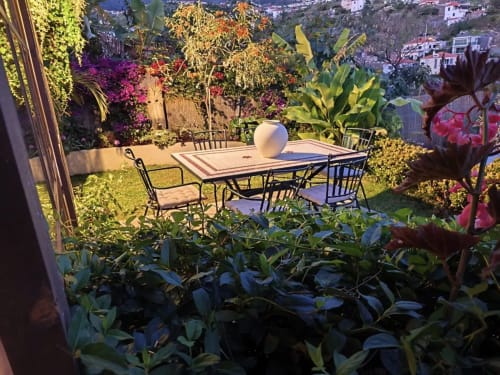 Zona de comedor en terraza de Les Terrasses Suites en Calheta con mesas, sillas y vistas al exuberante jardín con vistas a la costa.