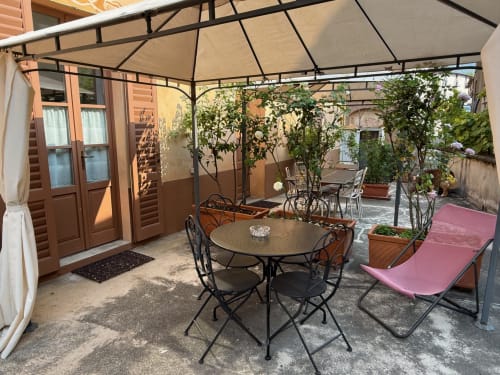 Patio coperto dell'appartamento La Rosa a Ponte In Valtellina con tavolo da pranzo, sedie e piante rampicanti sotto pergolato