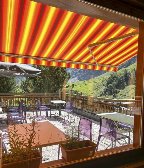 Auvent aux rayures rouge et jaune couvrant la terrasse extérieure des Bouquetins à Zinal avec vue sur les montagnes