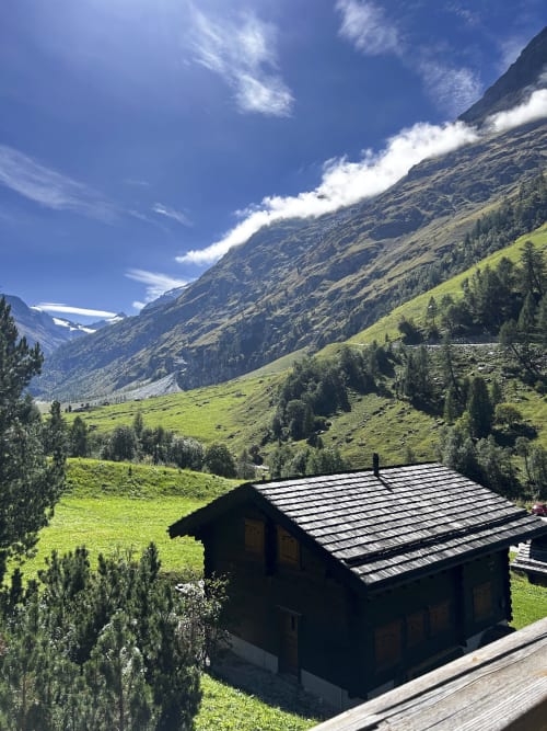 Chalet alpin traditionnel de l'Hôtel les Bouquetins à Zinal, entouré de prairies verdoyantes et de pics montagneux