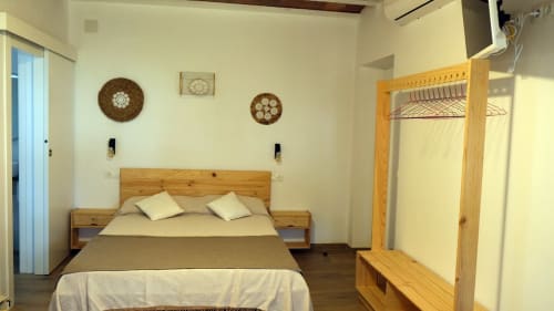 Dormitorio luminoso en Cal Xot B&B en Poble Nou con cama de madera, almohadas blancas, armario y relojes decorativos de pared