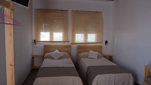 Dos camas individuales en una habitación luminosa del Cal Xot B&B en Poble Nou con cabeceros de madera y ventanas con contraventanas