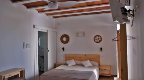 Dormitorio luminoso en Cal Xot B&B en Poble Nou con cama de madera, almohadas blancas, vigas vistas y adornos decorativos en las paredes