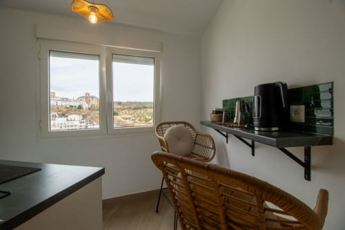 Modern kitchen-living area in Setenil de las Bodegas loft with mountain views through windows, rattan chairs, black shelving,