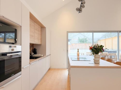 Moderne Küche mit weißen Schränken, Holzakzenten und Inseltheke mit Blick auf Essbereich und Garten
