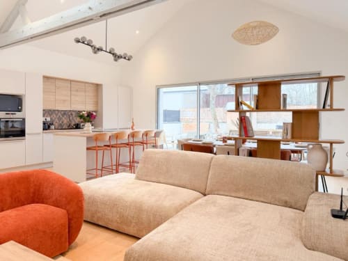 Modernes offenes Wohnzimmer mit Beige-Sofa, orangefarbenem Sessel, Küche und Holzregalen im Vindihouses Epinac BnB