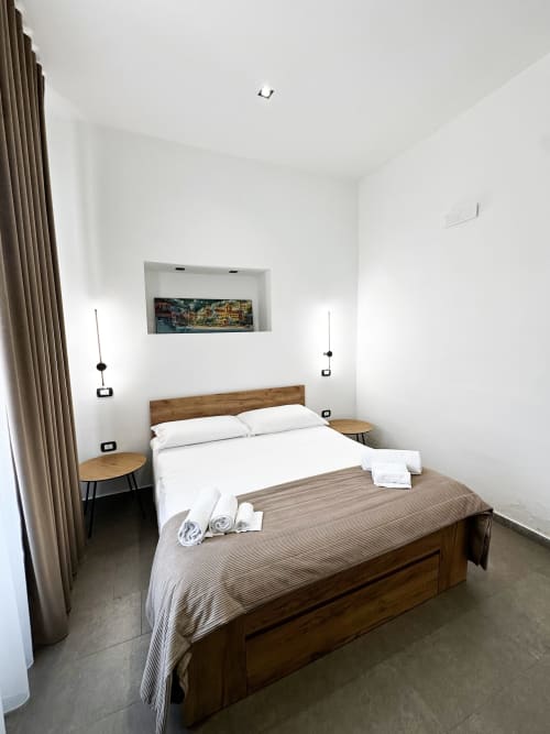 Camera moderna presso I colori di Napoli Napoli BnB con letto in legno, biancheria bianca, luci a sospensione e fotografie con vista sulla città