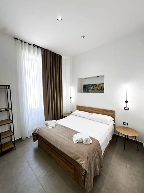 Camera moderna all'I colori di Napoli B&B di Napoli con letto in legno, biancheria bianca e tende con vista sulla città