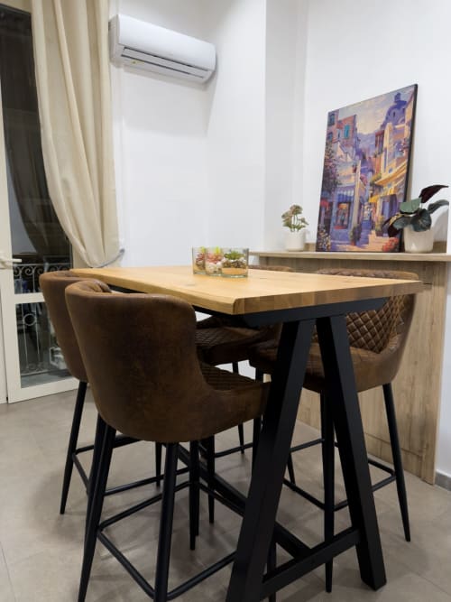 Spazio di lavoro moderno in un BnB a Napoli con tavolo bar in legno, sedie imbottite marrone, condizionatore e quadri colorati su pareti bianche