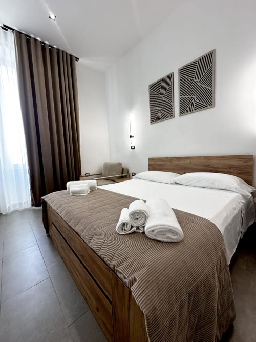 Camera moderna all'I colori di Napoli B&B a Napoli con letto in legno, biancheria bianca, asciugamani arrotolati e arte geometrica alle pareti
