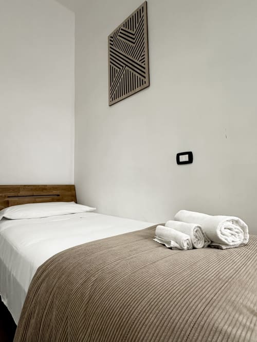 Camera minimalista presso I colori di Napoli B&B a Napoli con biancheria bianca, copriletto a righe, asciugamani arrotolati e parete geometrica