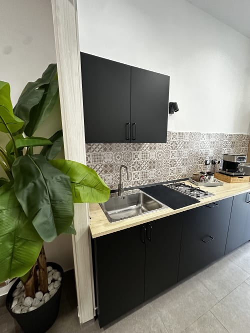 Piccola cucina moderna con mobili neri, piano di lavoro in legno, fornello a gas, lavello e piastrelle decorate a I colori di Napoli