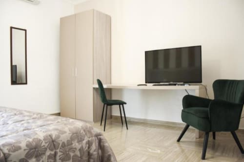 Camera moderna a Isernia con TV a schermo piatto, scrivania, poltrona verde e armadio in legno chiaro