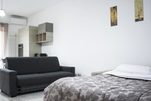 Moderno monolocale a Iserna con divano nero, letto matrimoniale con biancheria fantasia, scaffali a parete e vista sulla città