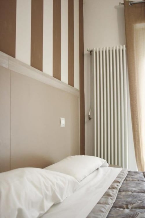 Camera da letto moderna nell'appartamento di Isernia con parete a righe, biancheria bianca e radiatore verticale