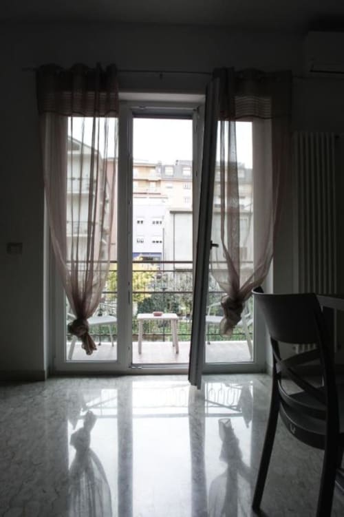 Ingresso luminoso di appartamento con porte-finestre aperte, vista sul balcone della città di Isernia, tende trasparenti, pavimenti lucidati, moderno