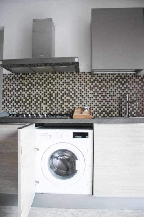 Cucina moderna con rivestimento a mosaico, lavatrice integrata, cappa aspirante e top in acciaio inox nella Suite Ambra