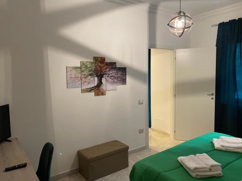 Camera da letto luminosa e moderna nella suite Giada, Isernia con letto verde, opera d'arte con alberi, lampada a sospensione e tende scure
