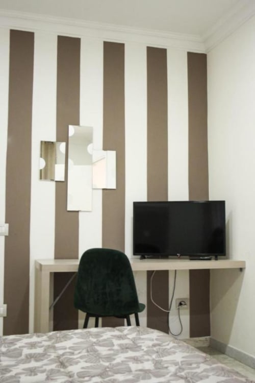 Camera da letto moderna con zona di lavoro, parete rigata, TV a schermo piatto, sedia da scrivania e biancheria con motivi nell'appartamento Giada di Suite in