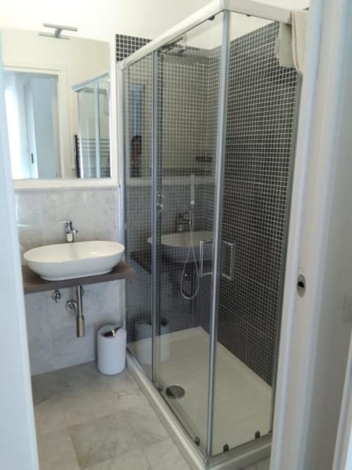 Bagno moderno con lavabo a cascata, ampia doccia in vetro con piastrelle mosaico scure e vanity bianco nell'appartamento Ematite