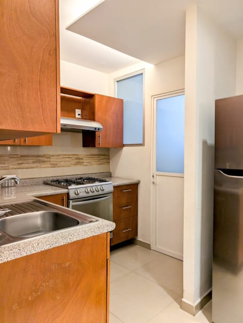 Cocina moderna con gabinetes de madera, encimeras de granito, estufa de gas y electrodomésticos de acero inoxidable en el apartamento Casa Donceles