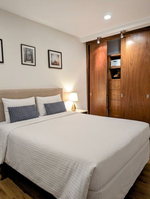 Dormitorio moderno en Casa Donceles, México con cama queen, almohadas geométricas, armario de madera y cuadros en la pared