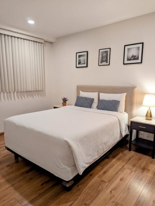 Recámara moderna en Casa Donceles en Ciudad de México con cama queen, cabecera beige, piso de madera y tres cuadros enmarcados