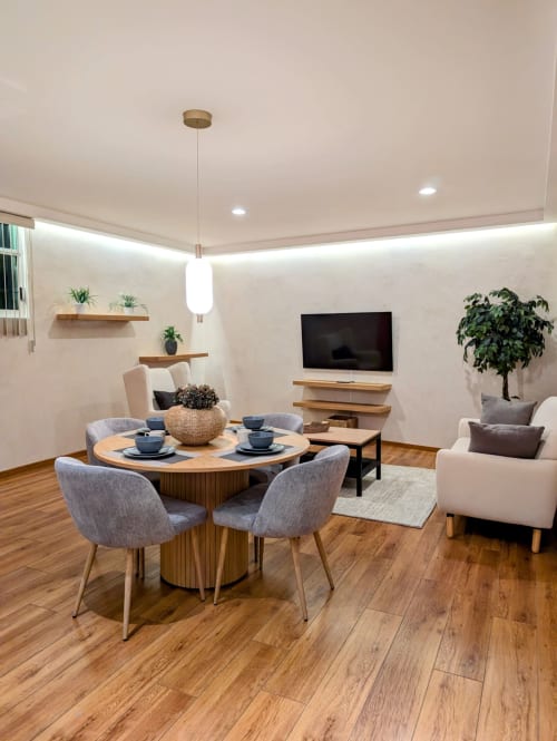 Sala moderna del apartamento Casa Donceles en Ciudad de México con mesa redonda, sillas grises, televisor, pisos de madera y plantas