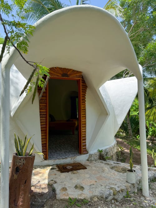 Entrada de domo geodésico blanco en el hostal Cayuco Maya en Bacalar, México con puerta de madera y jardín tropical