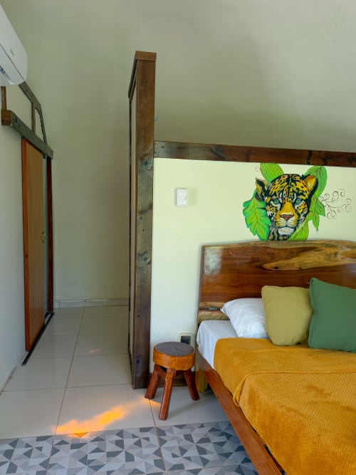 Acogedora habitación en el hostal Cayuco Maya de Bacalar con cama de madera, cojines coloridos y arte de leopardo en la pared