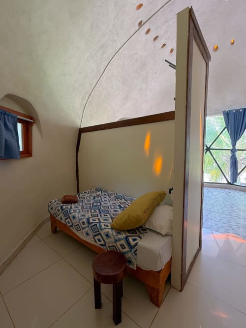 Acogedora habitación en domo geodésico del hostal Cayuco Maya, Bacalar, con cama con dosel, almohada amarilla y vista al jardín desde la ventana
