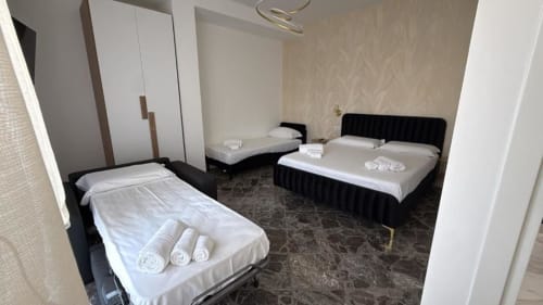 Ampia camera da letto nell'appartamento Newhouse Cavour Deluxe di Bari, con tre letti neri con biancheria bianca e asciugamani arrotolati
