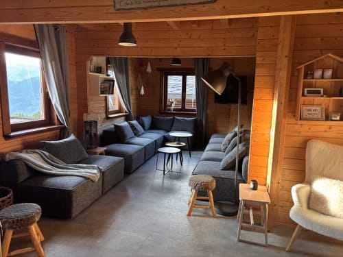 Salon chaleureux du chalet alpin avec vue montagne, sièges bleu-gris, poutres bois et équipements modernes aux Chalets