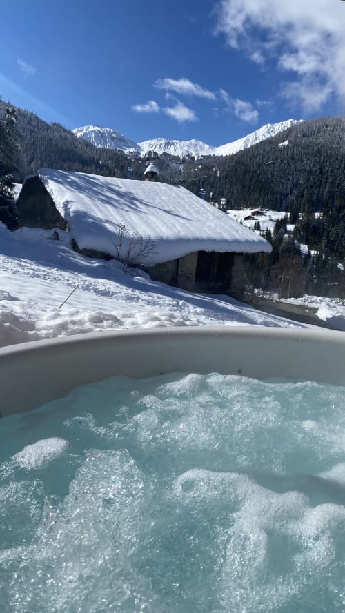 Jacuzzi fumant avec vue sur chalet enneigé et montagnes sommées de neige aux Chalets d'Aline, La Plagne Tarentaise