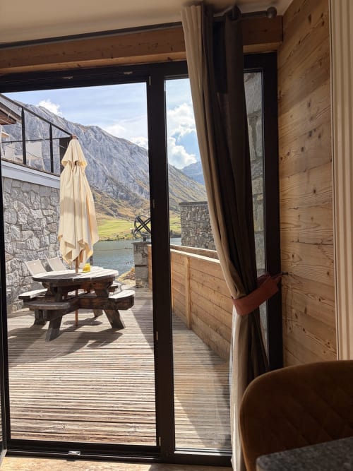 Terrasse du Tignes Lake Lodge avec parasol, table de pique-nique et vue panoramique sur le lac entouré de montagnes alpines