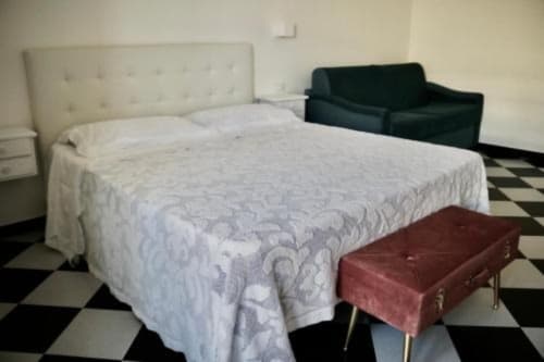 Camera doppia presso l'hotel Palazzo di Donna con letto trapuntato bianco, testata color crema, divano nero e panca bordeaux