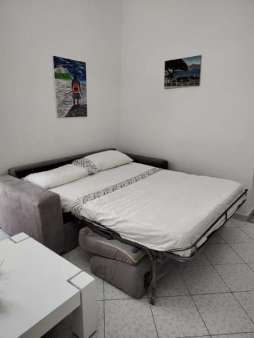 Divano letto grigio nella camera dell'hotel Palazzo di Donna con biancheria bianca e foto costiere alle pareti