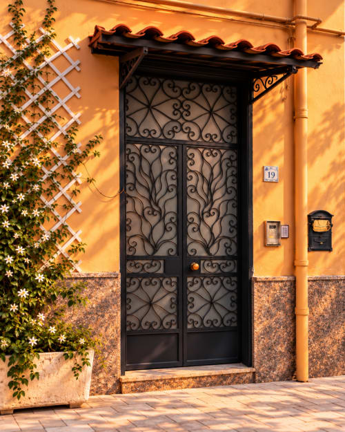 Ornate black iron door at Palazzo di Donna hotel in Italy, with yellow stucco wall and flowering vines