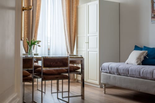 Modern bedroom at UrbanFlat Roma with desk, bed with blue pillows, golden curtains, and city views from window