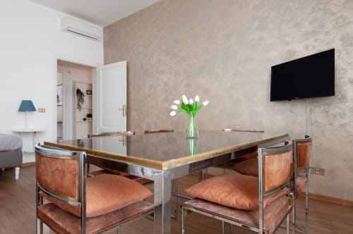 Modern UrbanFlat Roma apartment dining area with glass table, leather chairs, fresh flowers, wall-mounted TV, and