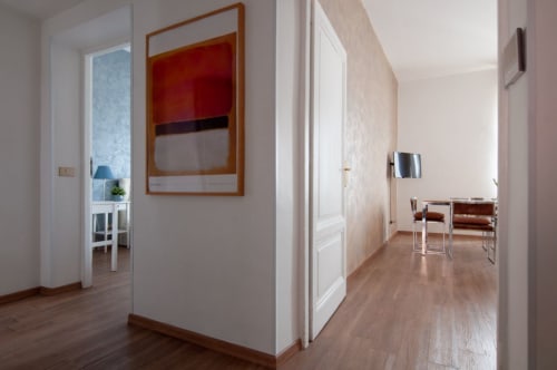 Modern hallway in UrbanFlat Roma apartment with wooden flooring, white walls, contemporary artwork, and open doors leading to