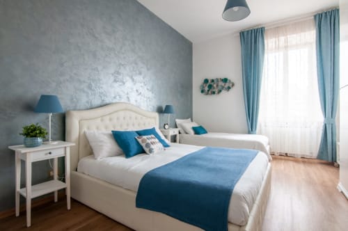 Modern bedroom at UrbanFlat Roma with two beds, blue accents, gray textured wall, and city view windows