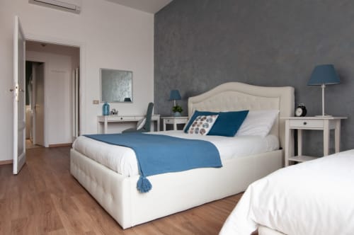Modern bedroom at UrbanFlat Roma with cream upholstered bed, blue accents, white nightstands, and hardwood floors