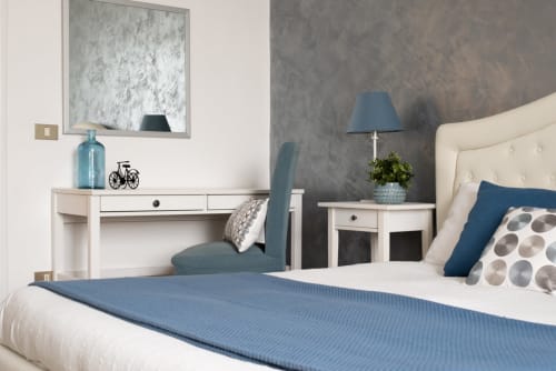 Modern bedroom at UrbanFlat Roma with blue accents, white furniture, desk, and city apartment amenities