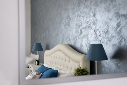 UrbanFlat Roma apartment bedroom with cream tufted headboard, blue lamps, and textured gray wall