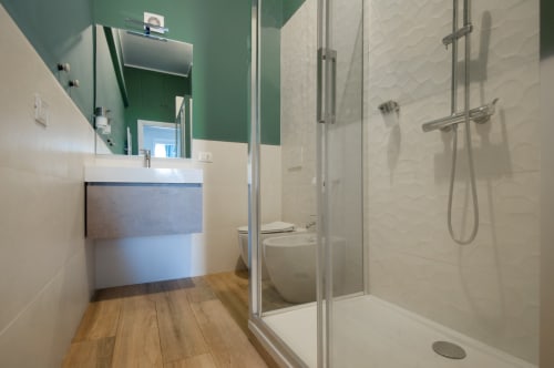 Modern bathroom in UrbanFlat Roma apartment with green accent wall, floating vanity, walk-in shower, and wood-look flooring