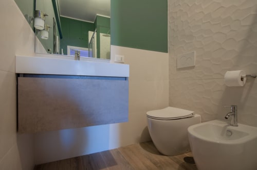 Modern bathroom in UrbanFlat Roma with white sink, toilet, bidet, and blue-accented vanity cabinet