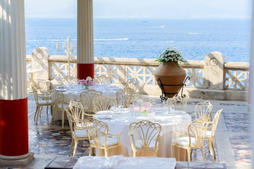 Elegant seaside dining terrace at Palazzo di Donna with white tablecloths, ornate chairs, and Mediterranean Sea views from