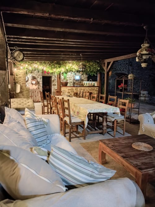 Rustic stone cottage terrace with lounge seating, dining tables, and chairs under pergola roof at French villa