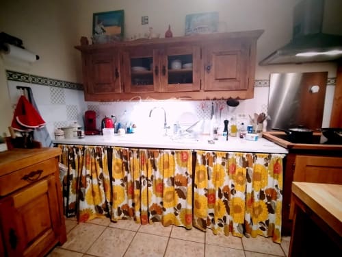 Spacious cottage kitchen with wooden cabinets, white countertop, and yellow floral curtains, Gagnières, South of France